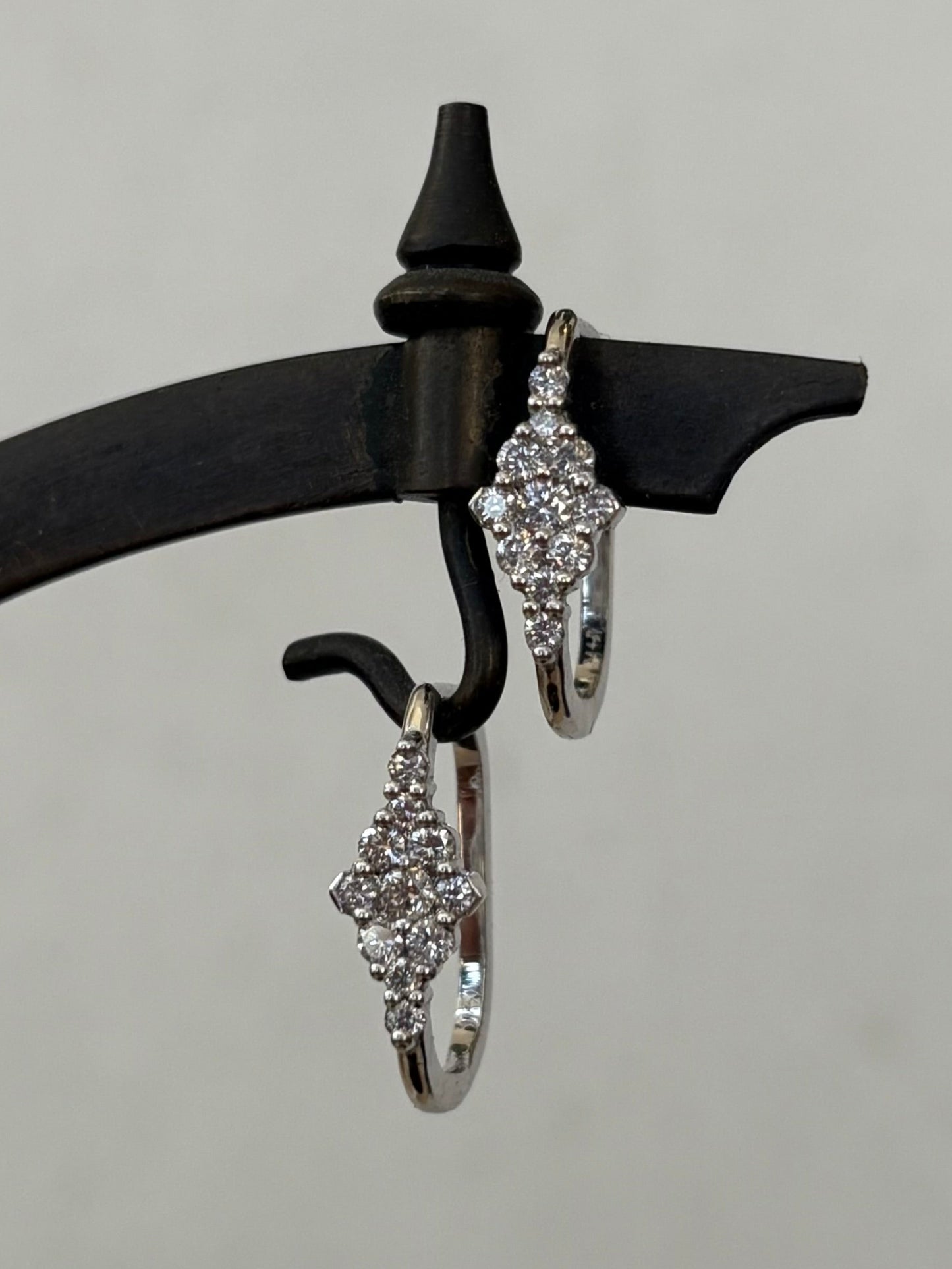Pair of white gold hoop earrings with diamonds stones on a black hanger against a gray background