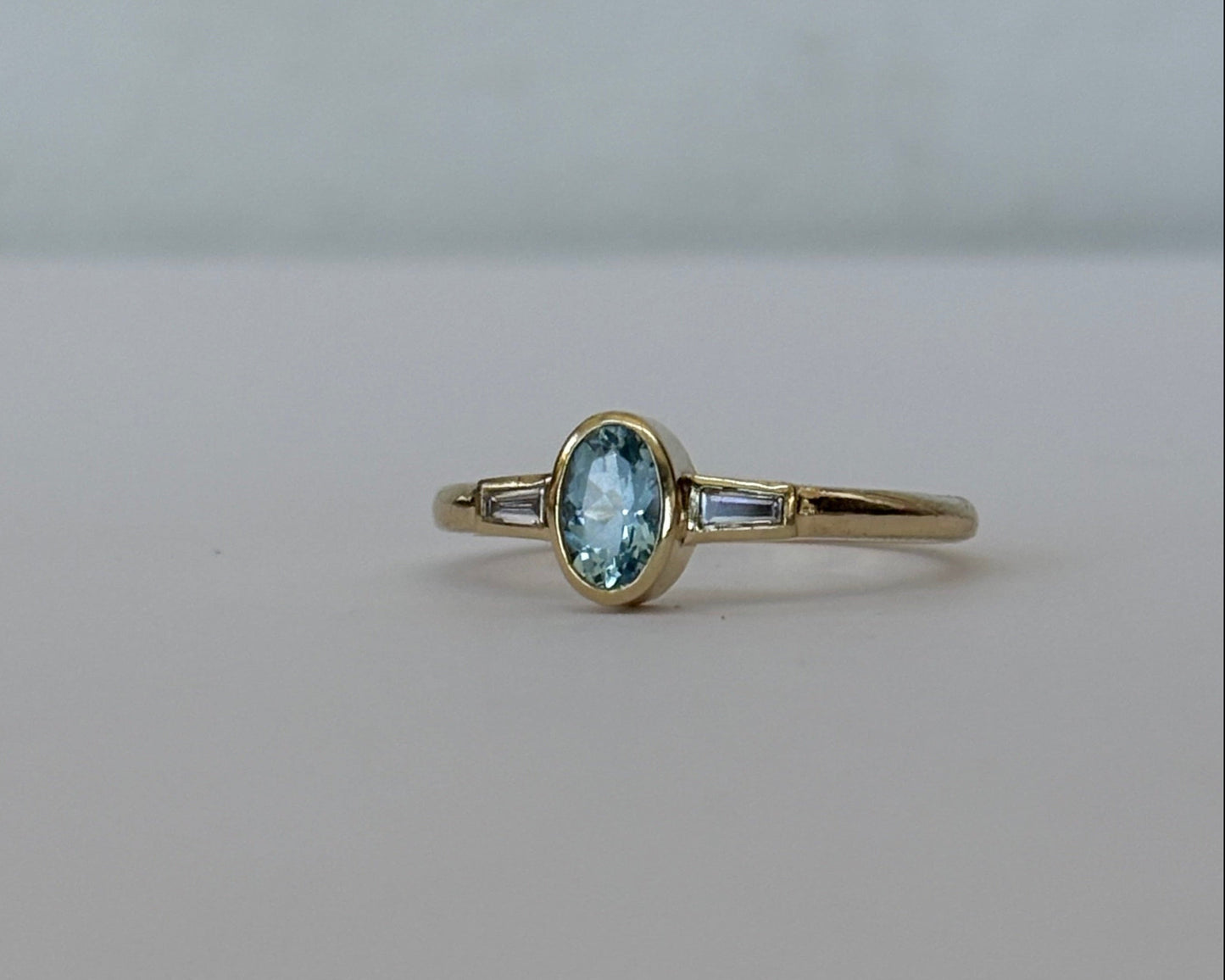 A gold ring featuring an oval-cut light blue gemstone, shown against a plain light gray background.