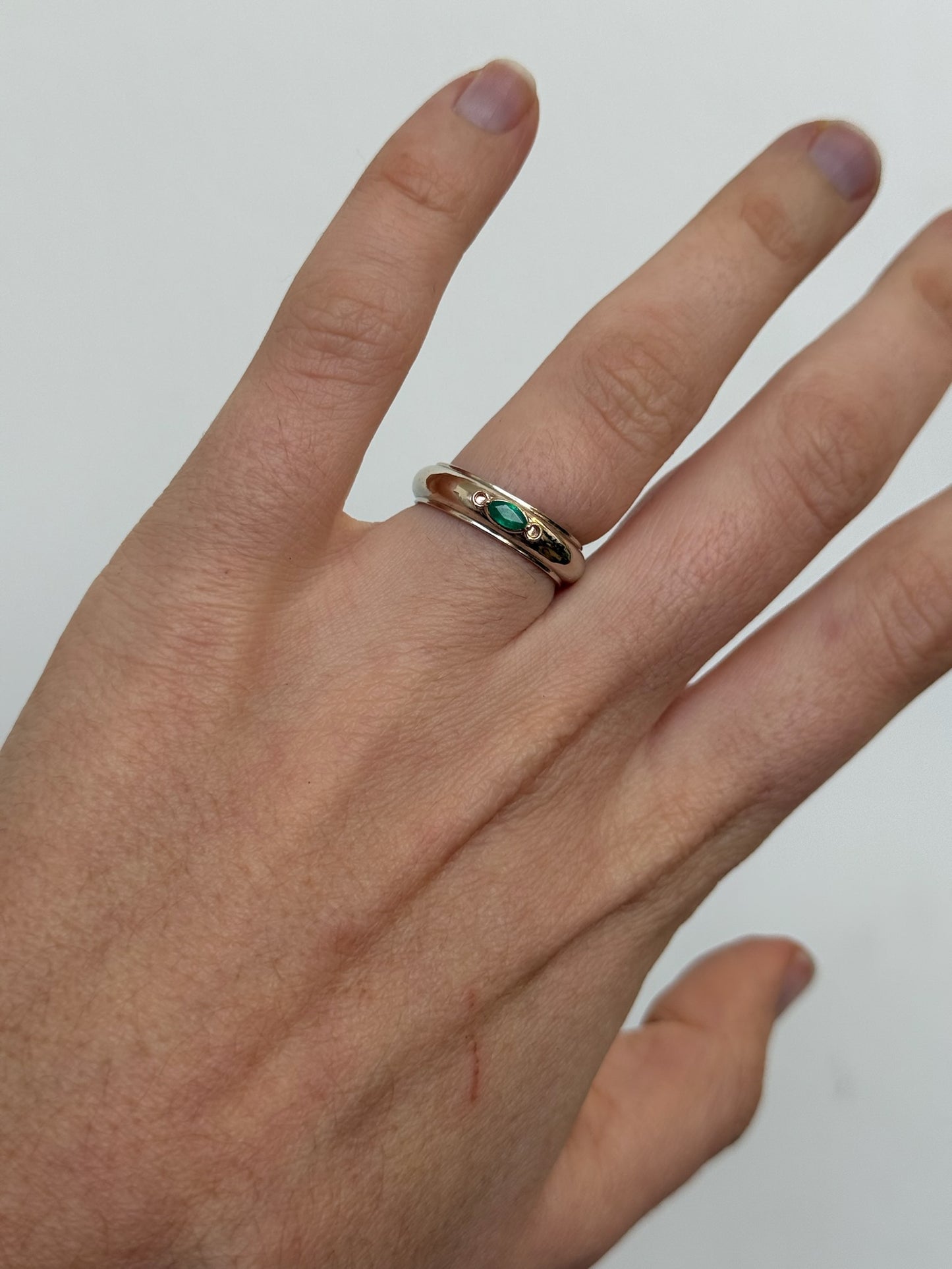 Hand wearing a white gold ring with a green EMERALD on a plain background
