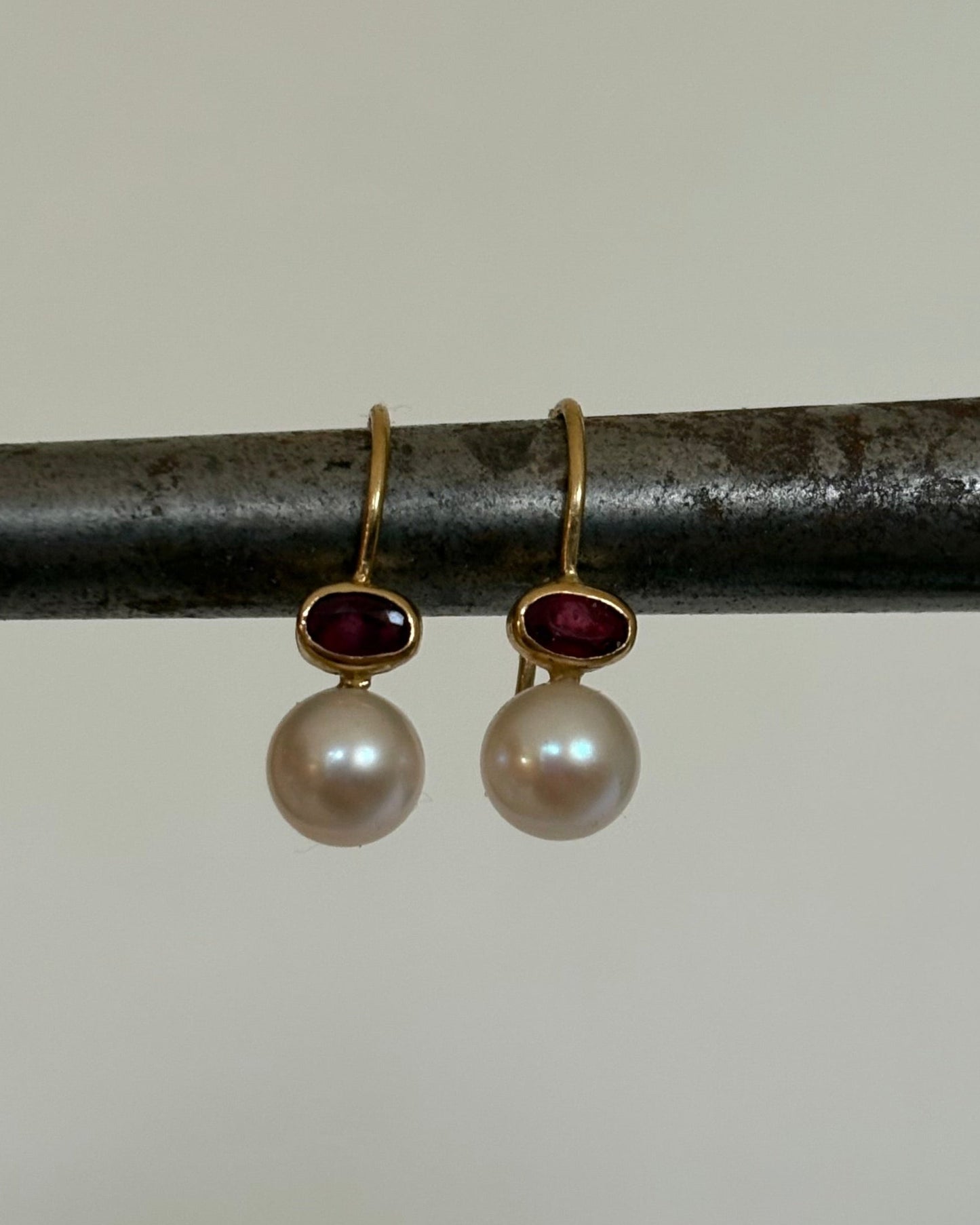 Pair of gold earrings with pearls and ruby gemstones on a metal rod.