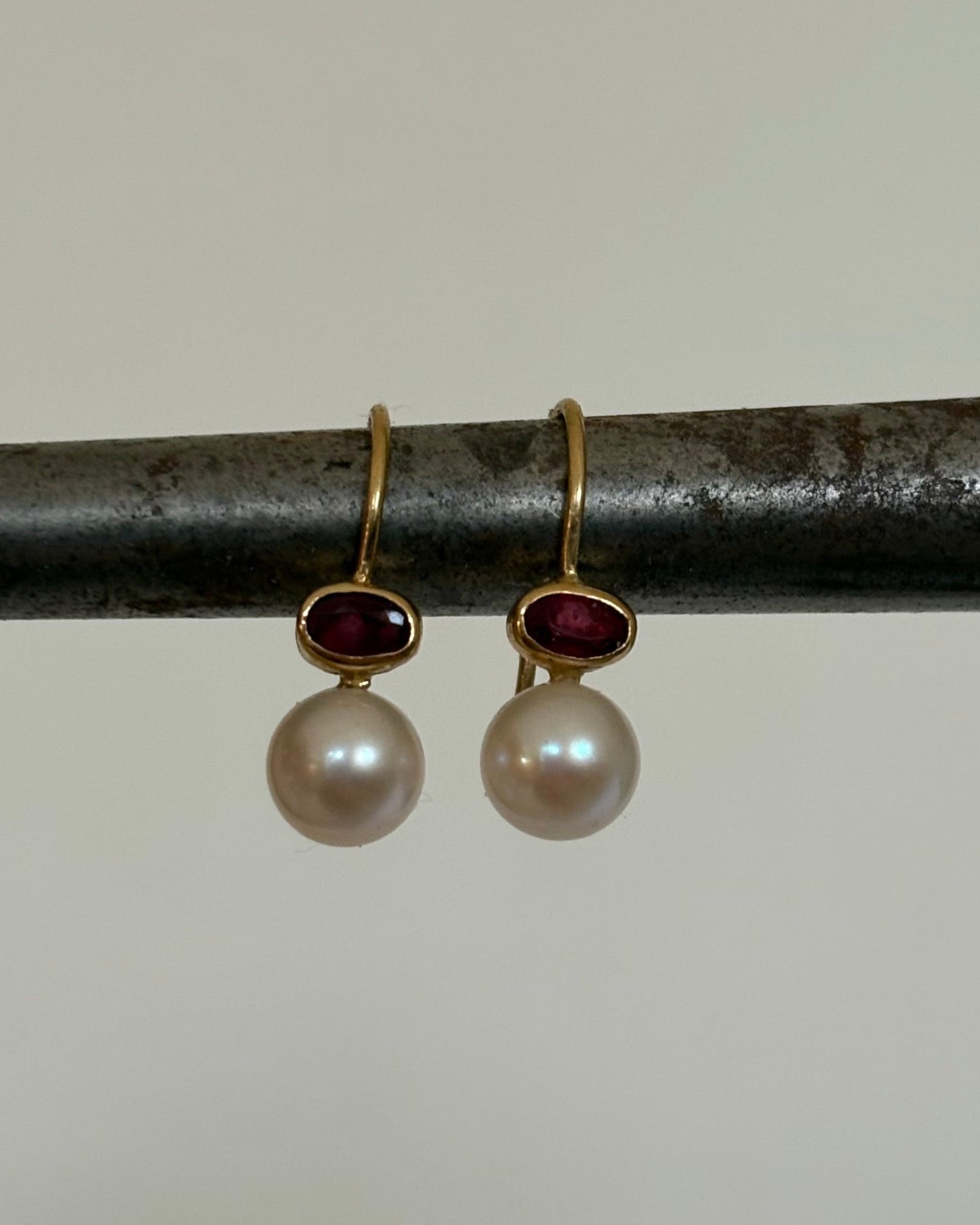 Pair of gold earrings with pearls and ruby gemstones on a metal rod.