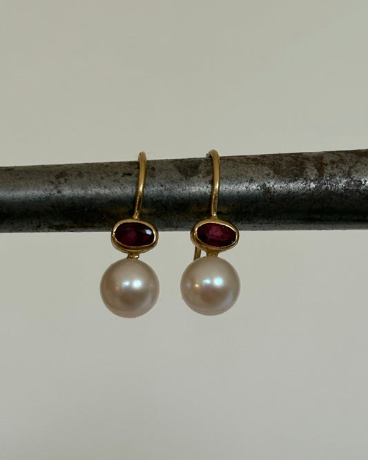 Pair of gold earrings with pearls and ruby gemstones on a metal rod.